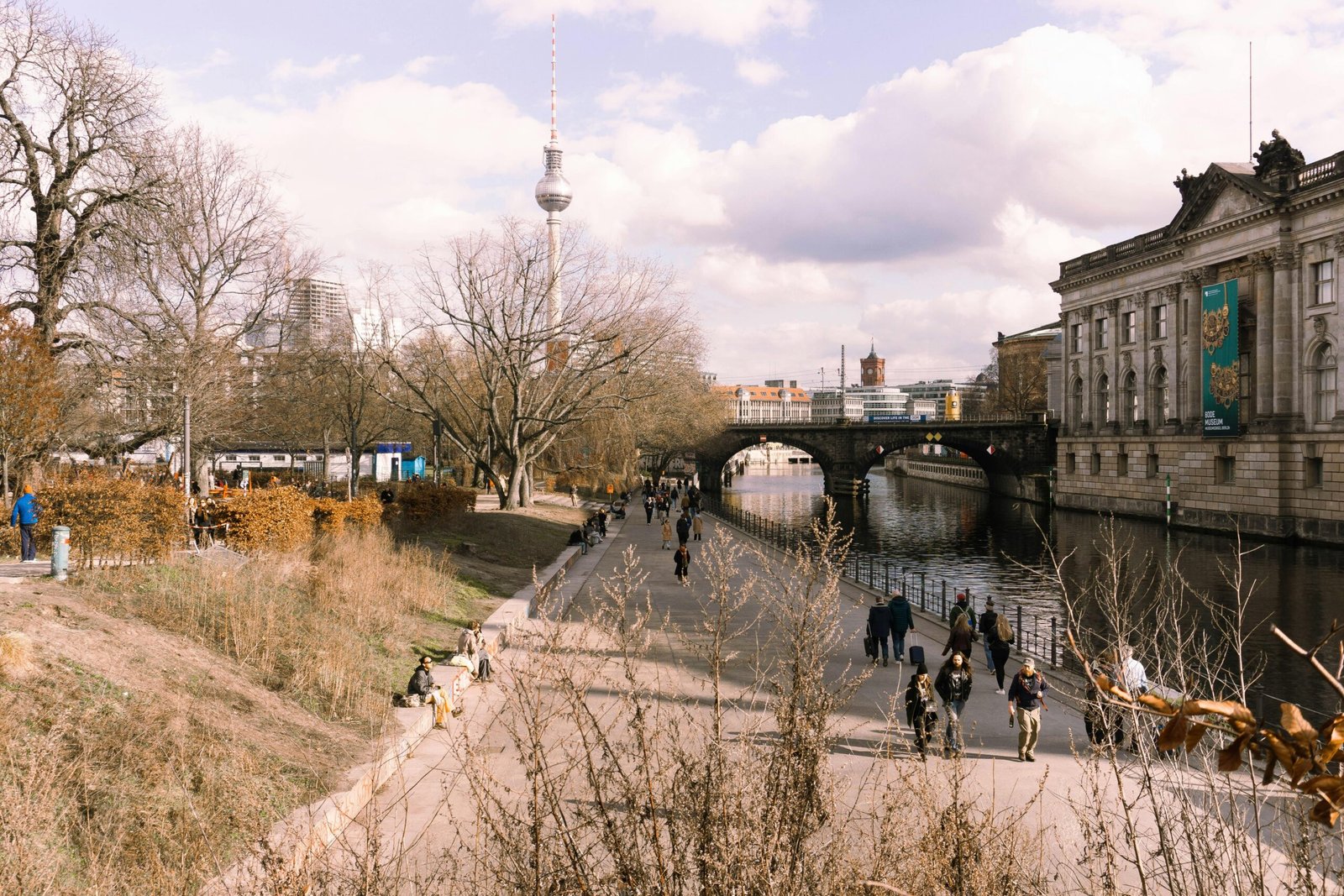 Scenic view of Berlin with the TV Tower, river, and people strolling. Perfect blend of nature and city.